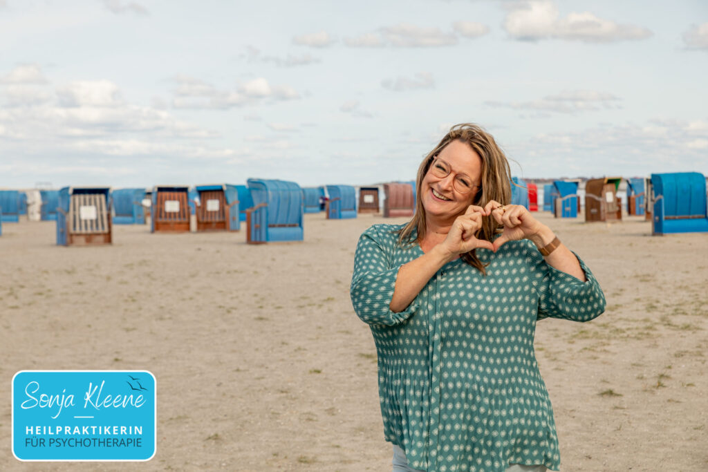Sonja Kleene am Strand macht mit den Händen eine Herzgeste